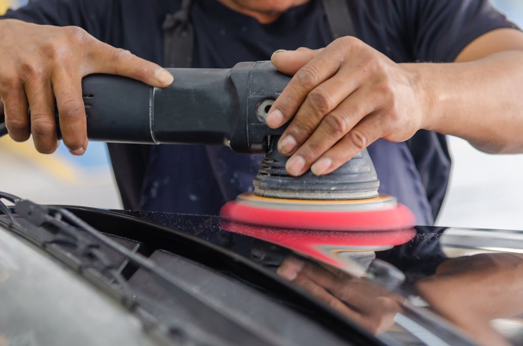 Close-up of a mechanic polishing a car with an electric buffer tool.