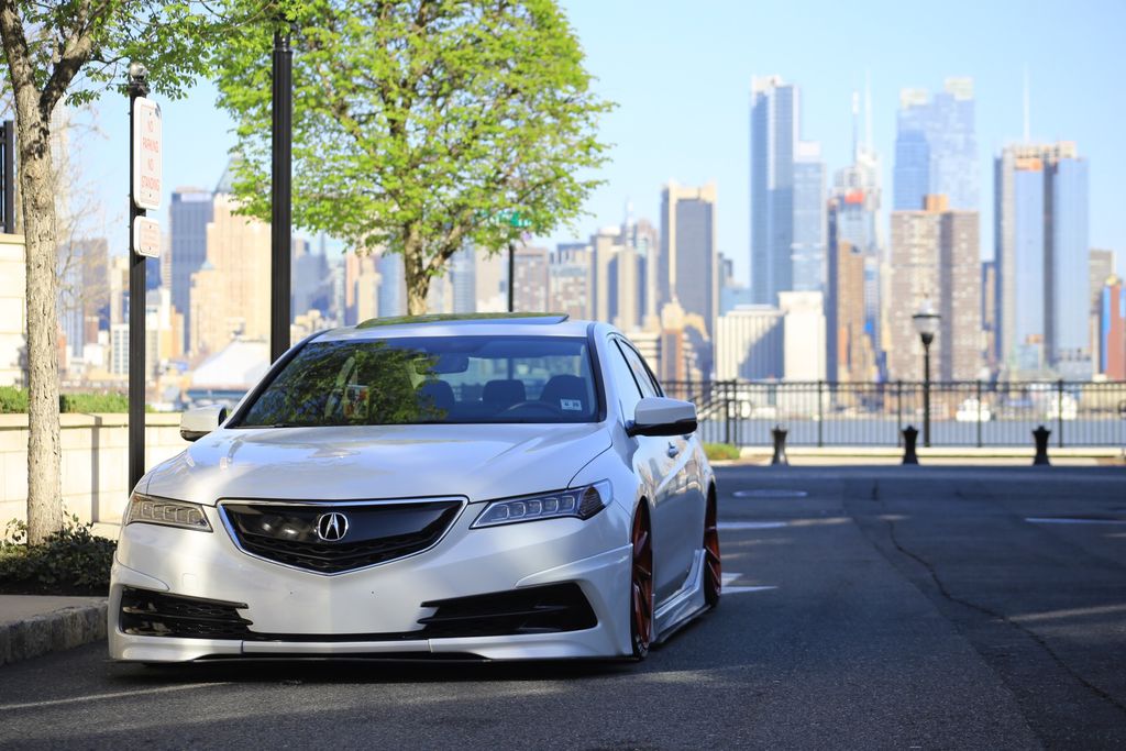 A customized silver Acura parked with a city skyline backdrop, showcasing urban car culture.