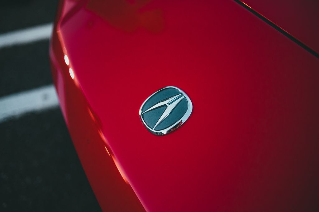 A detailed close-up of a red car hood featuring a shiny metallic emblem, captured outdoors.