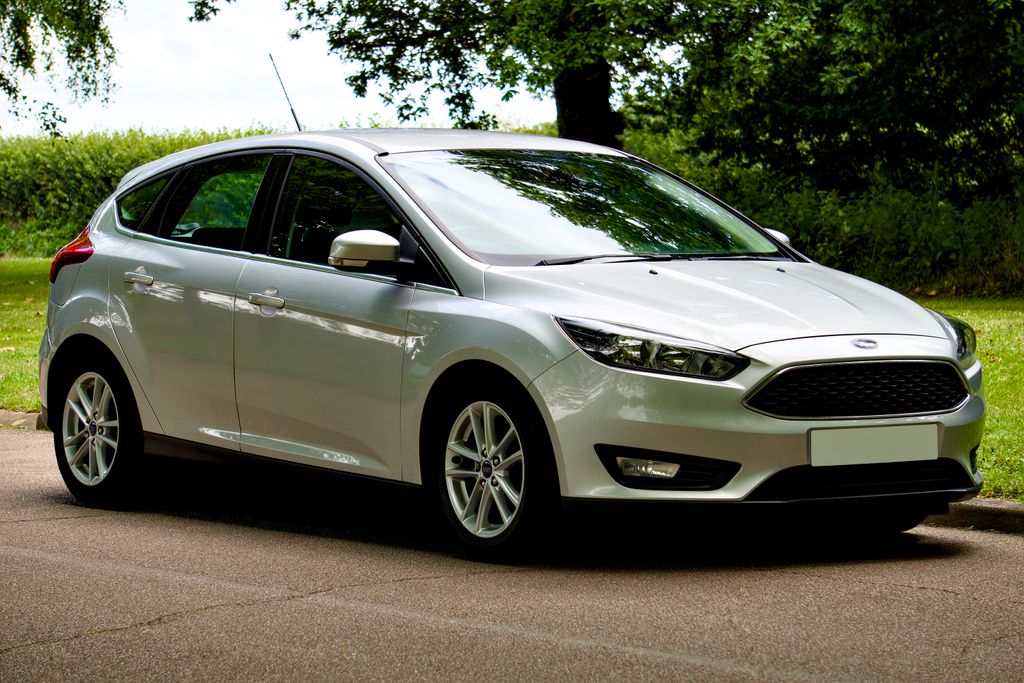 A sleek silver Ford Focus hatchback parked on a sunny day, with a scenic green background.