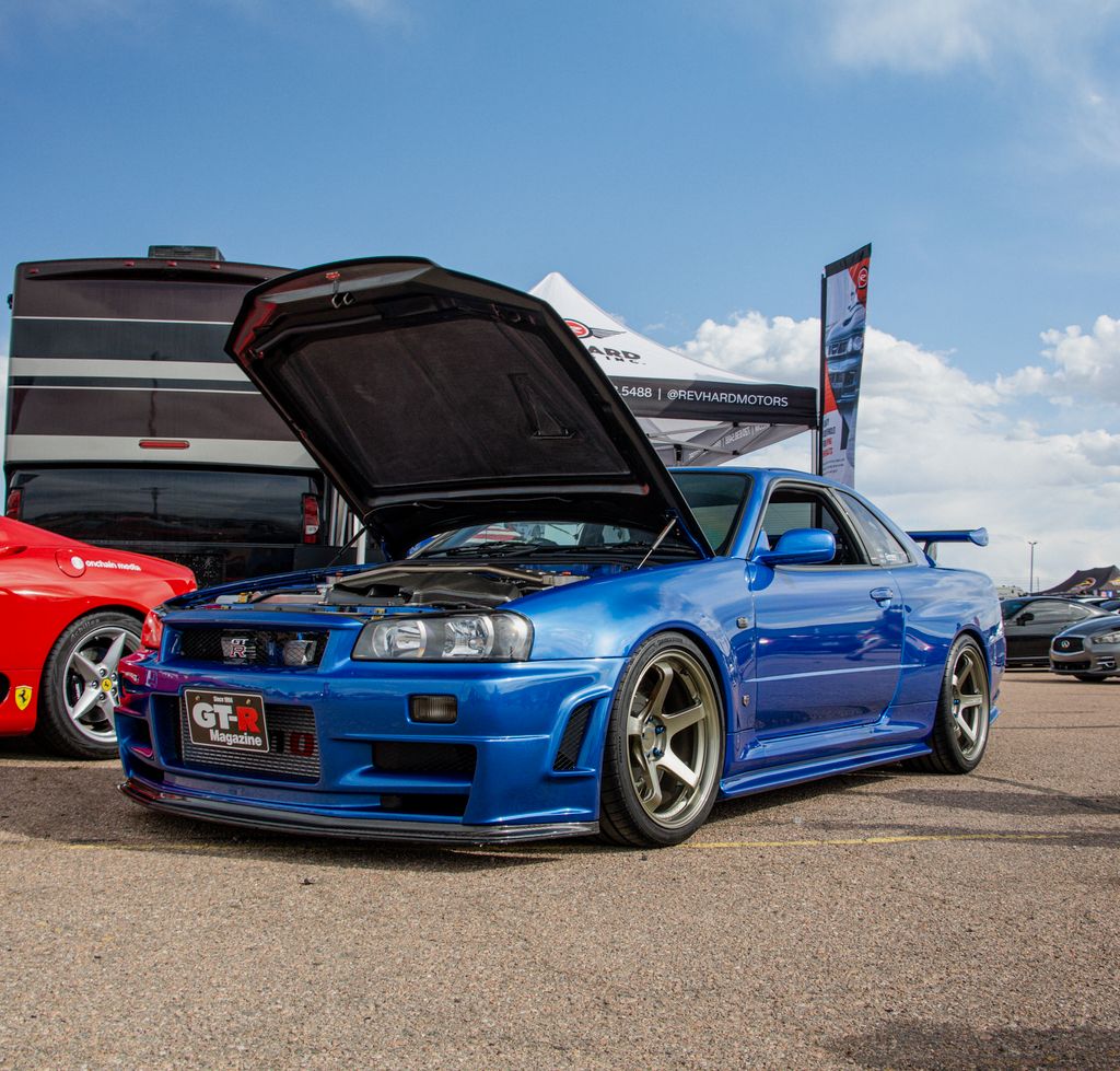 A striking blue Nissan Skyline R34 displayed with an open hood at a car show in Colorado.