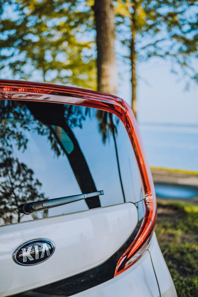 Close-up of car rear with logo and nature reflection in glass, outdoors.
