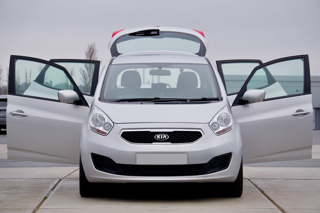 Front view of a silver Kia car with all doors open, parked on pavement.