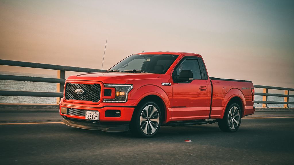 Red Ford F-150 truck driving on a bridge during sunset. Sleek and modern vehicle on the move.